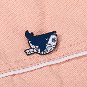 Close-up van een blauwe walvis emaille speld met tekst WHALE.SHIT op een roze canvas achtergrond