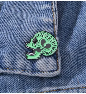 Dettaglio di una spilla a teschio verde con scritta Overthinking su tessuto denim