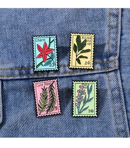Detail view of four floral stamp enamel pins on blue denim fabric with unique phrases
