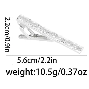 Polished silver tie clip with ornate scroll pattern engraving on a white background