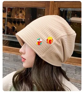 Dettaglio berretto beige in maglia con spillette smaltate a tema calza e regalo