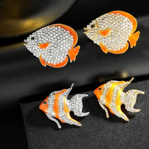Detailed view of fish-shaped brooches with orange enamel and crystal pavé on black leather