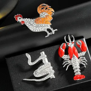 Dettaglio di spille smaltate a forma di gallo aragosta e serpente con strass scintillanti