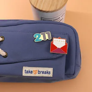 Success-themed enamel pins featuring 211 digits and red admission letter on blue canvas bag
