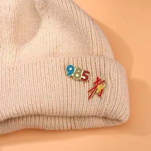 Detailed view of metal enamel badges with 985 and exam text on a beige knitted hat