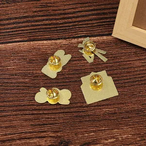 Set of four gold metal pins with butterfly clasps and textured back on wooden background