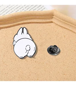 Detail shot of a cute white bunny enamel pin with a black butterfly clutch on a tray