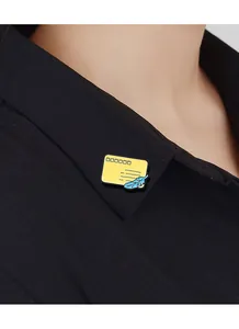 Detail shot of yellow envelope brooch with blue feather pinned on black shirt collar