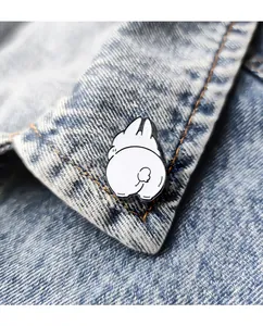 Close-up of a white enamel cartoon rabbit pin attached to a light blue denim jacket collar