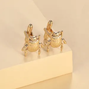 Macro view of gold beetle-shaped cufflinks with detailed wings on a neutral display pedestal