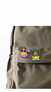 Cute cartoon pineapple enamel pins displayed on a khaki canvas backpack pocket for styling