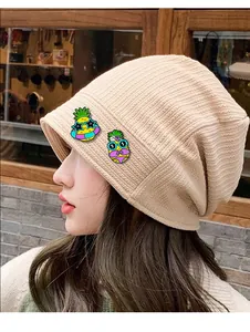 Détail du bonnet en maille côtelée beige orné de deux épingles à motif d'ananas mignon