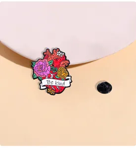 Detail einer Herz-Anatomie-Emaille-Anstecknadel mit Rosen und Be Kind Banner auf zartem Grund