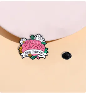 Detail der rosa Gehirn-Emaille-Anstecknadel mit Blumen und Be Kind To Your Mind Slogan