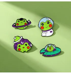 Detail von vier Cartoon-Frosch-Emaille-Pins mit Weltraum-Themen auf grünem Hintergrund