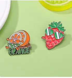 Détails de jolis pins émaillés en forme d'orange et de fraise sur fond frais