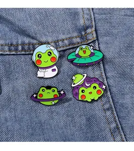 Detail von vier süßen Frosch-Astronauten-Emaille-Pins auf hellem Jeansstoff