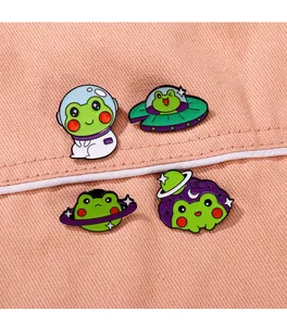 Detail von vier kreativen Cartoon-Frosch-Emaille-Pins auf rosa strukturiertem Stoff