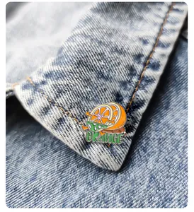 Gros plan d'un pin's émaillé en forme d'orange rigolote sur une veste en jean bleu