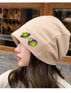 Detail von zwei süßen grünen Frosch-Emaille-Pins mit Weltraum-Elementen auf einer Strickmütze