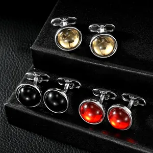 Close-up of three pairs of round crystal cufflinks in amber, black and red on a leather stand