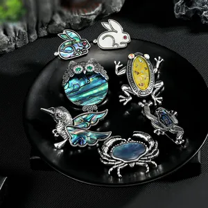 Makro-Detail von Tierbroschen mit farbigen Abalone-Schalen-Inlays auf dunklem Grund