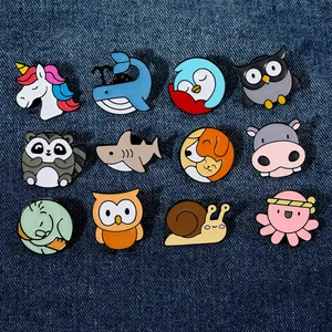 Detailed top view of 12 cartoon animal enamel pins laid out on dark blue denim fabric