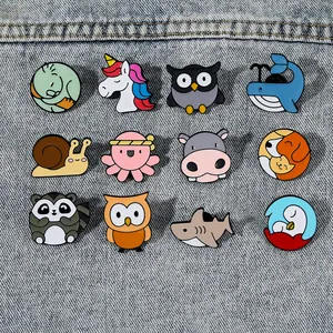 Set of 12 cartoon animal enamel pins including owls and snails on denim fabric background