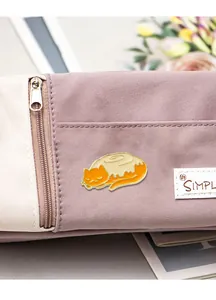 Detailed view of an orange cat on a cinnamon roll enamel pin on a purple fabric bag
