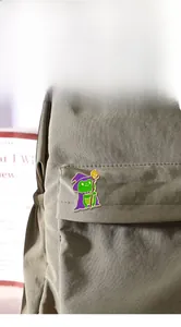 Dettaglio di una spilla smaltata a forma di rana mago su una borsa di tela verde