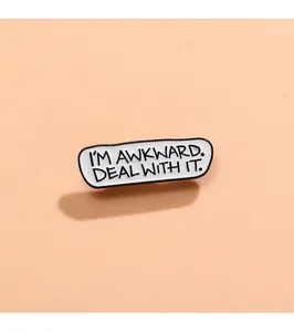 Makroaufnahme einer Emaille-Anstecknadel mit dem Text I'M AWKWARD DEAL WITH IT in Weiß und Schwarz