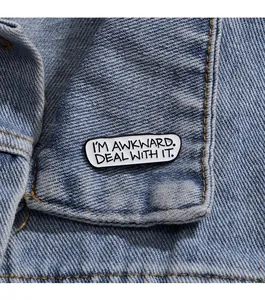Makroaufnahme der rechteckigen Emaille-Brosche mit Text I'm Awkward Deal With It auf Denim