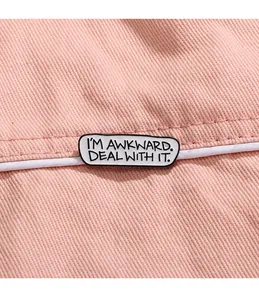 Detailansicht der 'I'M AWKWARD' Emaille-Anstecknadel auf rosa Stoffgewebe