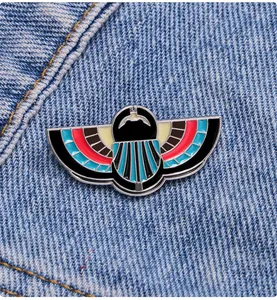 Detail of Egyptian style winged scarab enamel brooch on blue denim fabric background