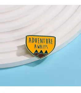 Détail d'un pin's émaillé jaune avec motif de montagne et texte Adventure Awaits