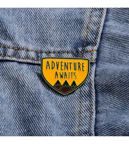 Détail de la broche émaillée jaune avec montagnes et texte Adventure Awaits sur denim