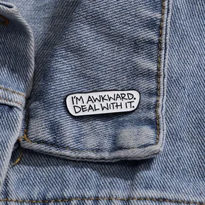 Minimalistische Emaille-Brosche mit Spruch auf einem blauen Denim-Jackenkragen