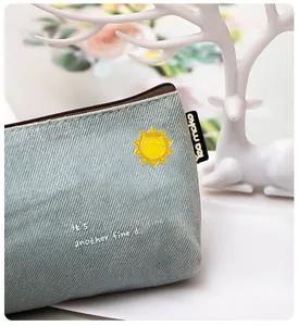 Détail du pin's soleil en émail sur une trousse en velours bleu avec texte fin