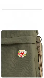 Broche en émail avec fleurs et champignons épinglée sur un sac en toile olive