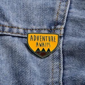 Broche émaillée montagne Adventure Awaits sur une veste en jean bleue