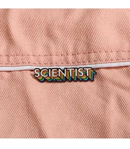 Makroaufnahme der bunten 'SCIENTIST' Emaille-Anstecknadel auf rosa Denim-Stofftextur