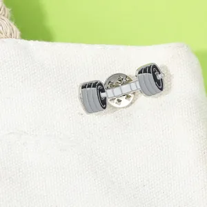 Macro detail of fitness barbell enamel pin attached to a white canvas texture bag