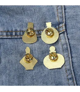Detail view of four gold butterfly clutch enamel pin backs on blue denim fabric