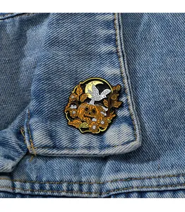 Dettaglio della spilla smaltata zucca e fantasma di Halloween su colletto in denim