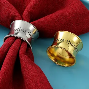 Detalle de servilleteros de metal con grabado Give Thanks y bordes perlados en tela