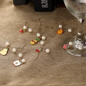 Detail of fruit charms on gold wine glass rings with pearls over rustic linen backdrop