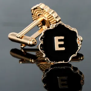 Detailed close-up of gold and black cufflinks featuring the letter E on a reflective surface