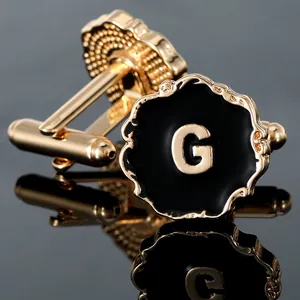 Macro shot of gold cufflink with black enamel disk and letter G on reflective base