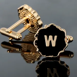 Macro view of gold-plated round cufflinks with letter W on a black reflective surface