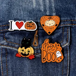Detail of four Halloween enamel pins with cat and pumpkin motifs on blue denim fabric